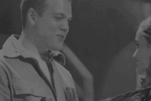 a gif of rachel zegler, josh andrés rivera, and tom blyth. the first half of the gif being josh and rachel staring at each other as rachel holds lucy gray's (the character she plays) guitar. the second half being tom blyth picking up rachel by surprise.